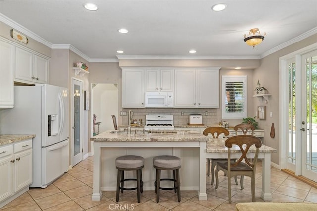 kitchen featuring an island with sink, backsplash, white appliances, crown molding, and light tile patterned floors