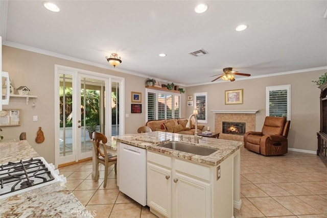 kitchen featuring white appliances, an island with sink, a sink, a glass covered fireplace, and crown molding