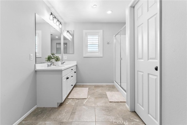 full bath with a sink, a stall shower, baseboards, and double vanity