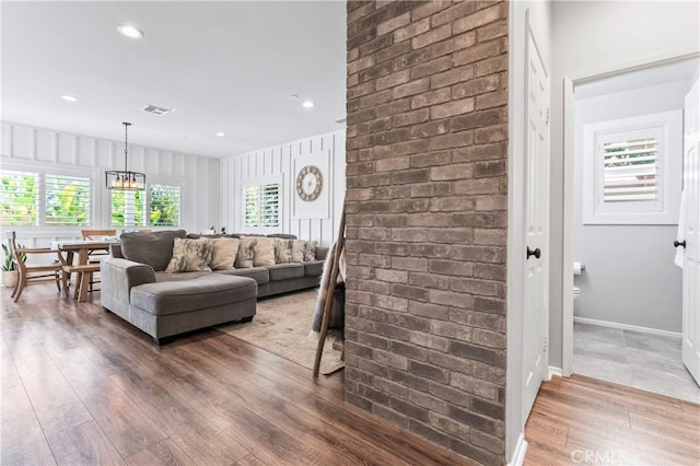 living area with visible vents, wood finished floors, brick wall, baseboards, and a chandelier