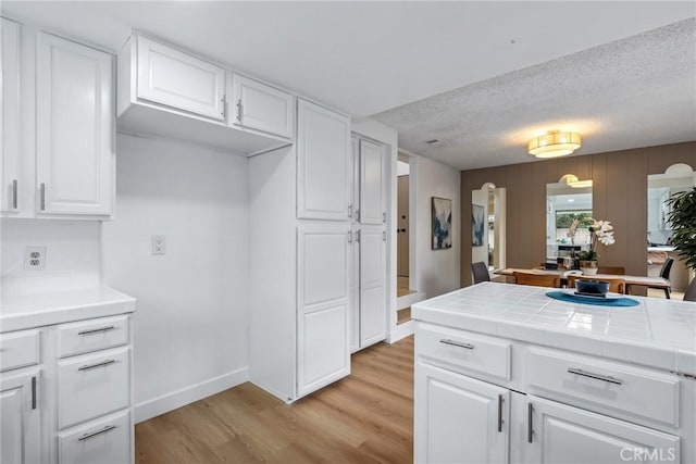 kitchen featuring a textured ceiling, arched walkways, white cabinets, light wood finished floors, and tile counters