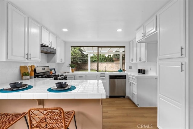 kitchen featuring under cabinet range hood, stainless steel appliances, a peninsula, and tile counters