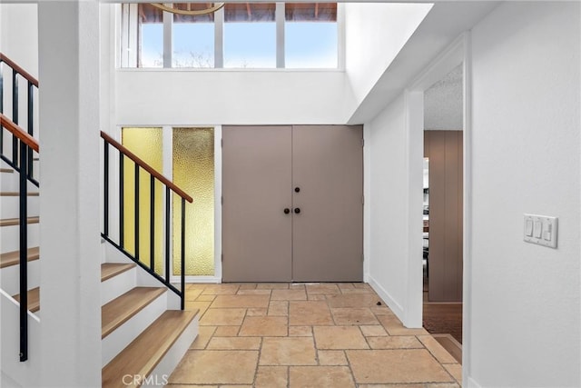 entrance foyer featuring stone tile floors, stairway, and a high ceiling