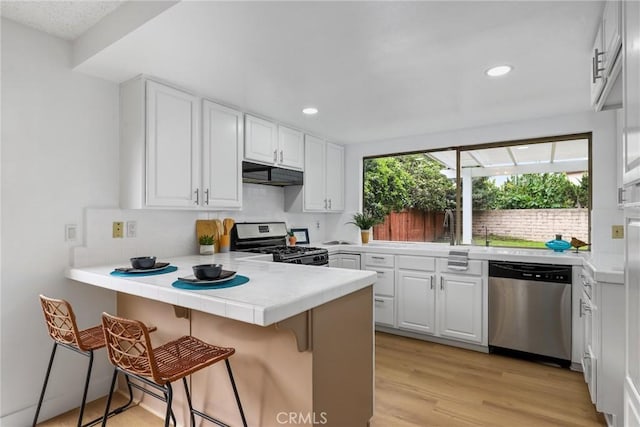 kitchen featuring a peninsula, recessed lighting, white cabinetry, under cabinet range hood, and appliances with stainless steel finishes