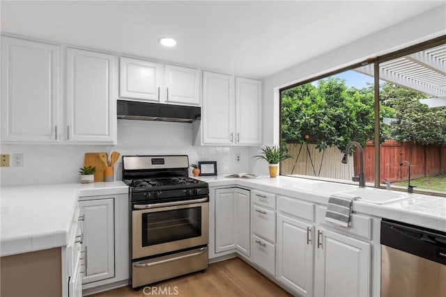 kitchen with under cabinet range hood, stainless steel appliances, tile counters, and white cabinetry