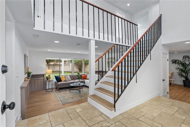 stairway with recessed lighting, baseboards, a towering ceiling, and stone tile flooring