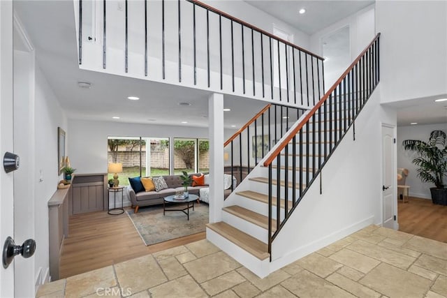 staircase with baseboards, recessed lighting, wood finished floors, and a towering ceiling