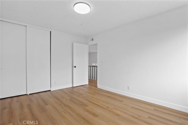 unfurnished bedroom featuring visible vents, baseboards, light wood-style flooring, a closet, and a textured ceiling