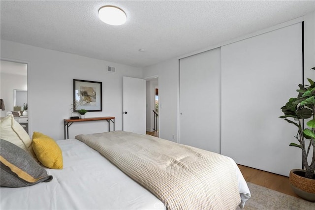 bedroom with wood finished floors, visible vents, a closet, and a textured ceiling