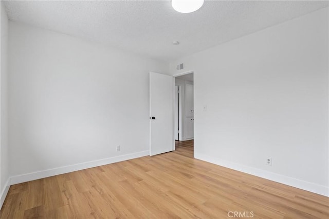 empty room featuring visible vents, baseboards, a textured ceiling, and light wood-style flooring