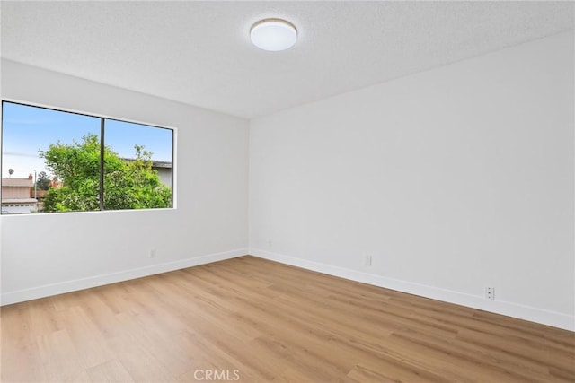 empty room with light wood-type flooring, baseboards, and a textured ceiling