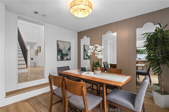 dining room with visible vents, a textured ceiling, stairs, and wood finished floors