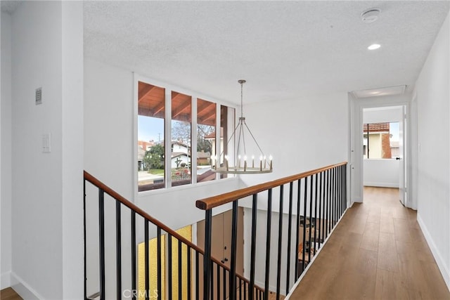 hallway featuring a textured ceiling, a notable chandelier, wood finished floors, and an upstairs landing