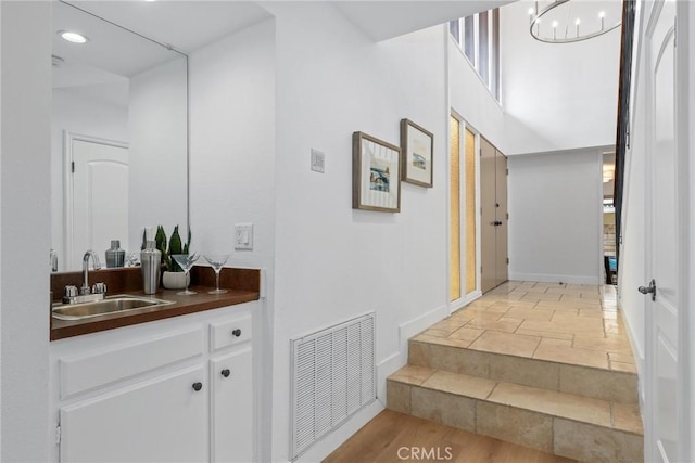 hallway with visible vents, stone tile flooring, baseboards, recessed lighting, and a sink