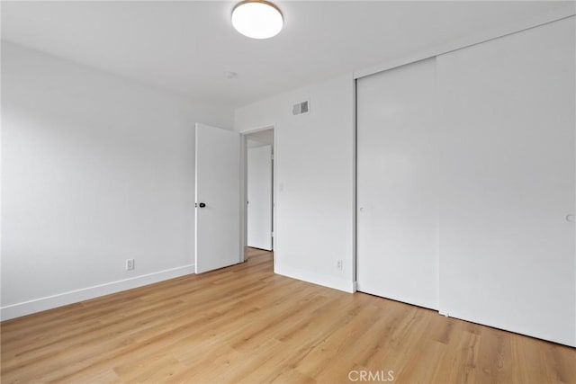 unfurnished bedroom with visible vents, light wood finished floors, baseboards, and a closet