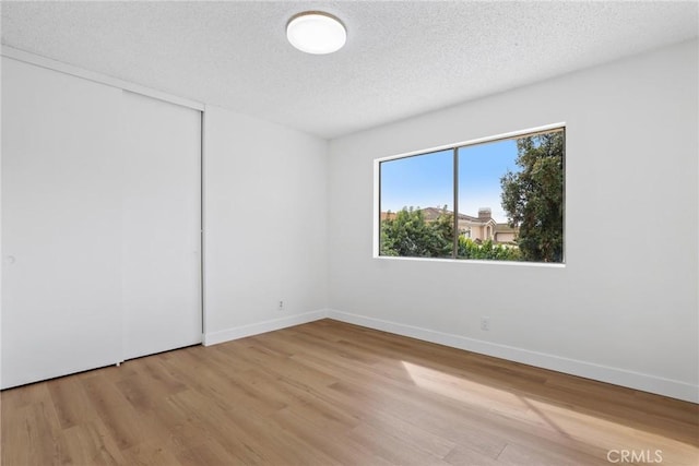 unfurnished room with baseboards, a textured ceiling, and wood finished floors