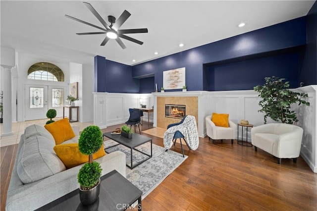 living area with a high end fireplace, a decorative wall, wood finished floors, and ornate columns