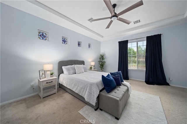 bedroom featuring a ceiling fan, baseboards, visible vents, a tray ceiling, and light carpet