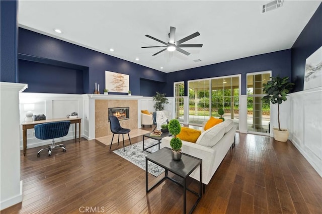 living room with visible vents, a ceiling fan, a tiled fireplace, wood finished floors, and a decorative wall