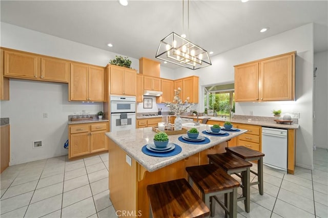 kitchen with under cabinet range hood, a kitchen island, double oven, and light tile patterned flooring