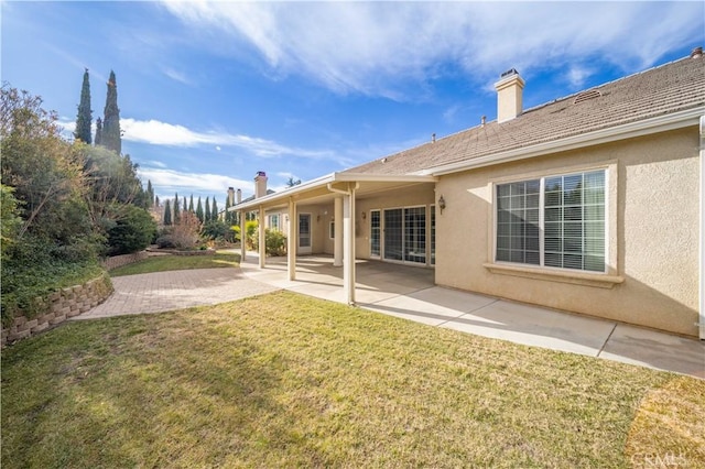 rear view of property with a patio area, a lawn, roof with shingles, and stucco siding