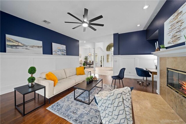 living room featuring visible vents, a fireplace, arched walkways, a decorative wall, and ceiling fan with notable chandelier