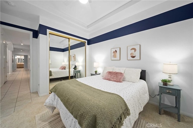 tiled bedroom with a tray ceiling, carpet flooring, baseboards, and a closet