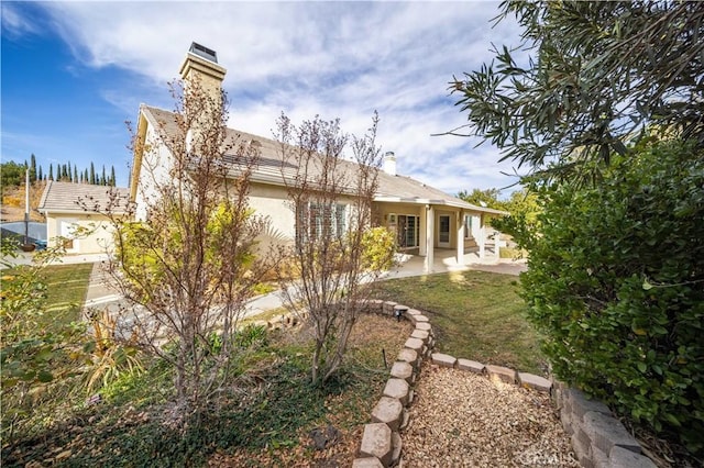 rear view of house featuring a patio area, a chimney, and stucco siding