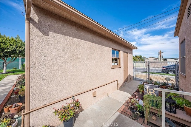 view of side of property with a gate, fence, and stucco siding