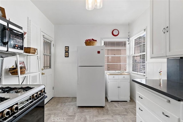 kitchen featuring dark countertops, freestanding refrigerator, gas range, white cabinetry, and stainless steel microwave