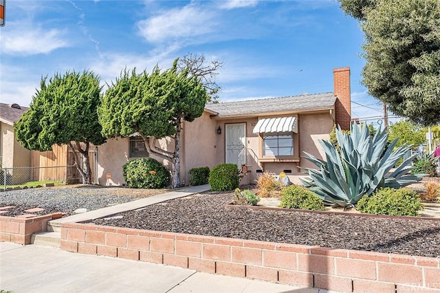 view of front of house featuring stucco siding, a chimney, and fence