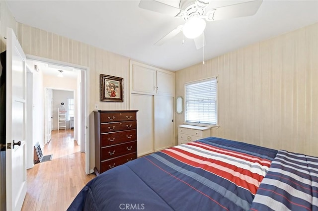 bedroom featuring a closet, light wood-style floors, a ceiling fan, and wallpapered walls