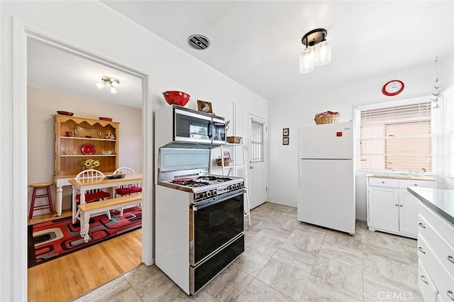 kitchen featuring stainless steel microwave, visible vents, freestanding refrigerator, white cabinets, and gas stove