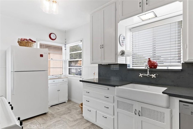 kitchen featuring decorative backsplash, a sink, dark countertops, freestanding refrigerator, and dishwashing machine