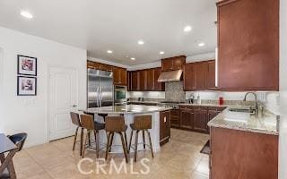 kitchen featuring a sink, under cabinet range hood, a kitchen island, appliances with stainless steel finishes, and a breakfast bar area