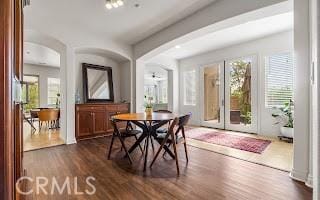 dining room with arched walkways, a healthy amount of sunlight, and dark wood finished floors