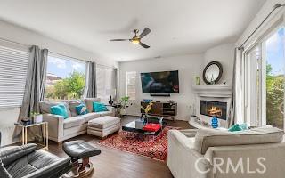 living room with wood finished floors, a glass covered fireplace, and a ceiling fan