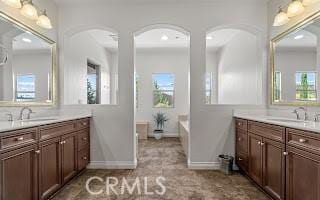 bathroom with two vanities, a bathtub, baseboards, and a sink