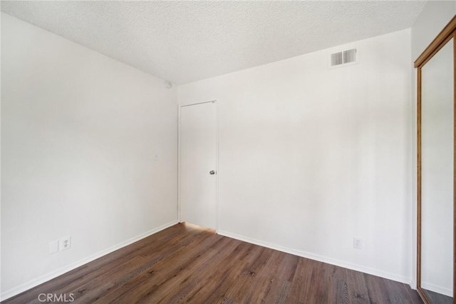 spare room with visible vents, a textured ceiling, dark wood-type flooring, and baseboards