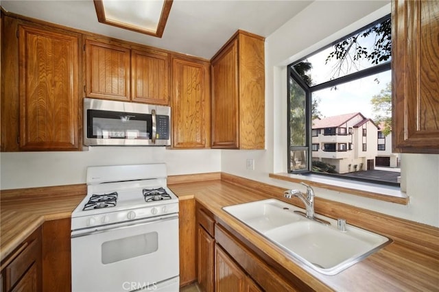 kitchen featuring brown cabinets, a sink, stainless steel microwave, white gas range oven, and light countertops