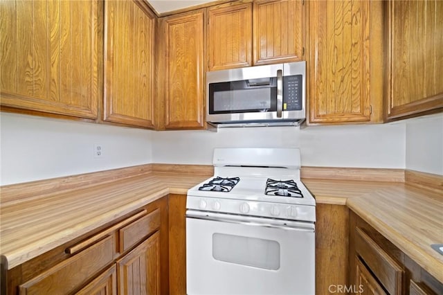 kitchen with white gas stove, stainless steel microwave, and brown cabinetry