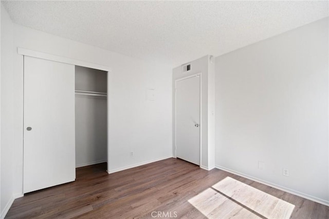 unfurnished bedroom with visible vents, baseboards, wood finished floors, a closet, and a textured ceiling