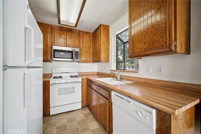 kitchen with a sink, white appliances, brown cabinetry, and light countertops