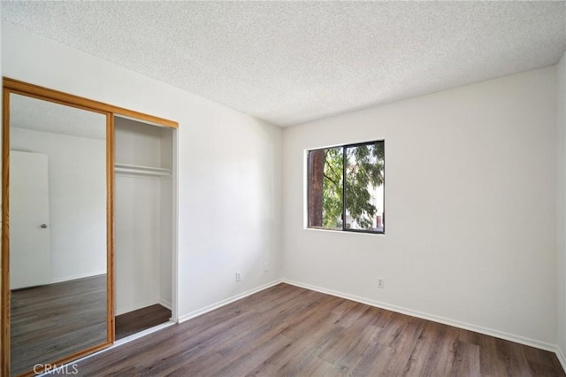 unfurnished bedroom featuring a closet, a textured ceiling, baseboards, and wood finished floors