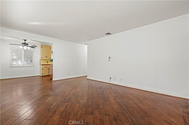 spare room with ceiling fan, visible vents, baseboards, and dark wood finished floors