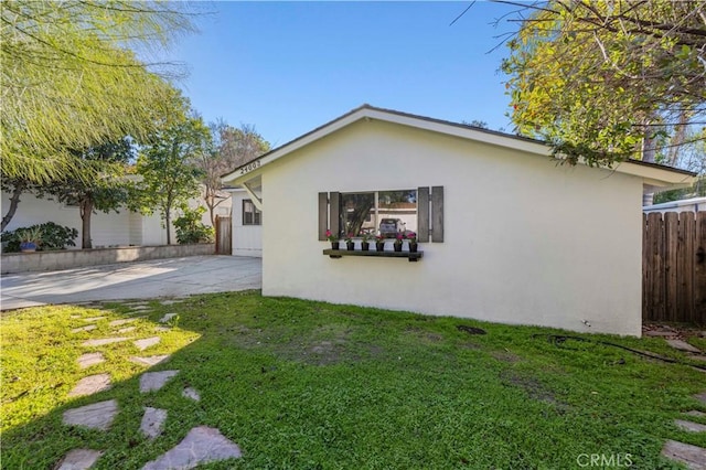 rear view of house featuring stucco siding, a yard, concrete driveway, and fence