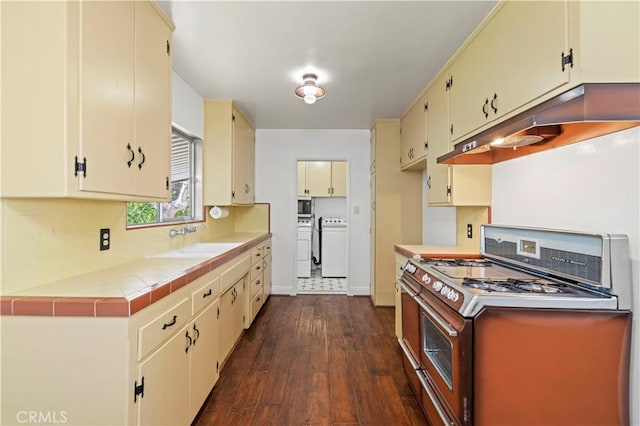 kitchen featuring under cabinet range hood, washing machine and dryer, cream cabinets, stainless steel appliances, and a sink