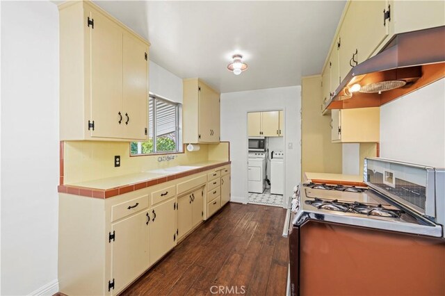 kitchen with cream cabinetry, a sink, dark wood finished floors, range with gas cooktop, and washing machine and clothes dryer