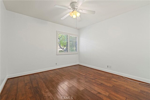 empty room featuring dark wood finished floors, a ceiling fan, and baseboards