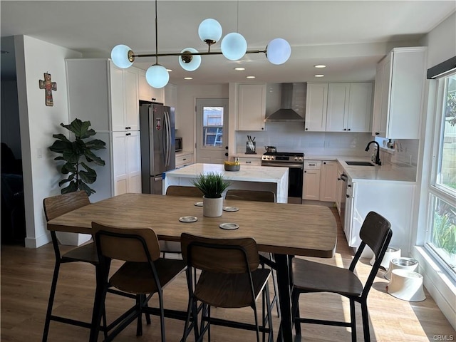 kitchen with a sink, wall chimney range hood, a kitchen island, appliances with stainless steel finishes, and light countertops